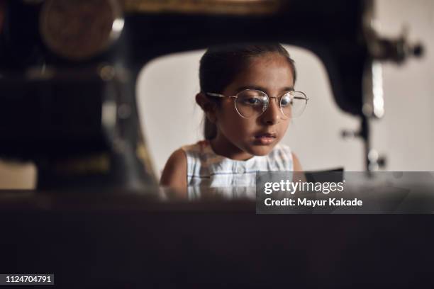 Young girl working on sewing machine wearing her Grandmother’s eyeglasses