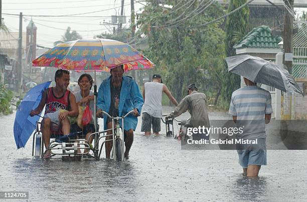 People ride and walk through a flooded street July 13, 2002 in Valenzuela, Philippines. Heavy rain from typhoon Halong flooded wide areas of Manila...