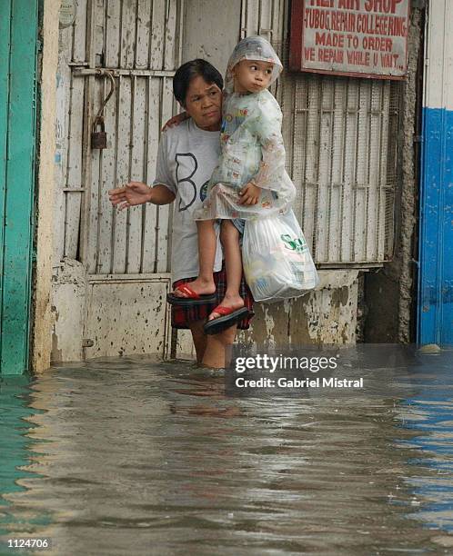 Woman carries her son as they walk through a flooded street July 13, 2002 in Valenzuela, Philippines. Heavy rain from typhoon Halong flooded wide...