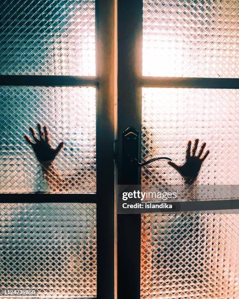 backlit silhouette of hands touching a glass door - locura fotografías e imágenes de stock