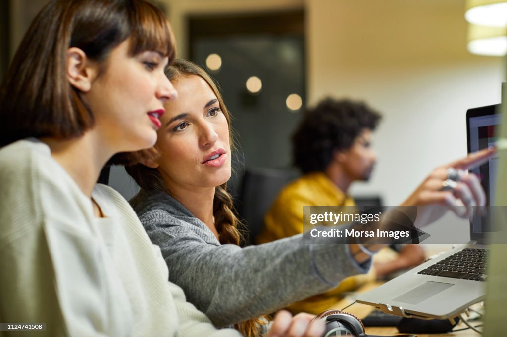 Coworkers discussing over computer in office