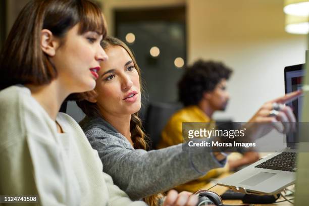 coworkers discussing over computer in office - nuova impresa foto e immagini stock