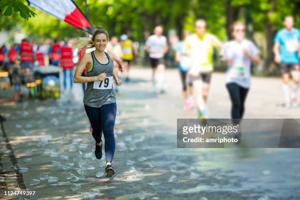 happy female marathon runner running over plastic cups - maratona imagens e fotografias de stock