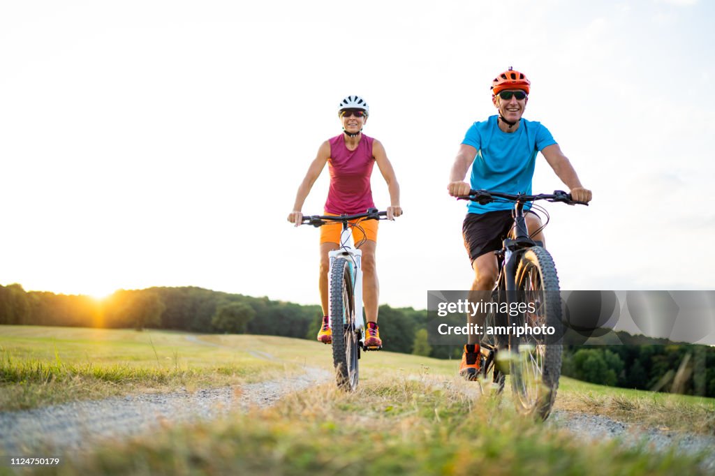 Casal de desportivo de 40-50 anos de idade ciclismo em bicicletas de montanha elétrica no meio rural