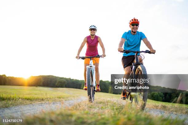 casal de desportivo de 40-50 anos de idade ciclismo em bicicletas de montanha elétrica no meio rural - exercise bike - fotografias e filmes do acervo