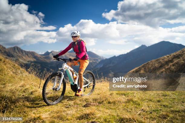 gelukkige vrouw op elektrische mountain bike hoge up in europese bergen - elektrische fiets stockfoto's en -beelden