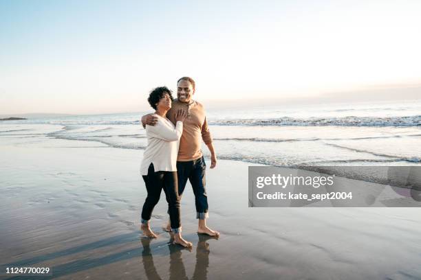 senior men walking with senior women on the beach - couple walking on beach stock pictures, royalty-free photos & images