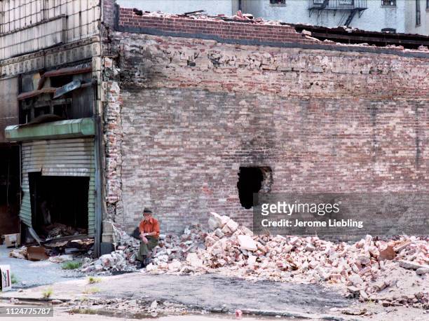 An unidentified elderly man sits in front of a bombed-out building surrounded by brick rubble in New York City's South Bronx neighborhood, New York,...