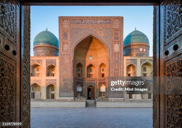 view into the courtyard and the decorated arch and minarets of a madrasa or mosque in bukhara city centre. - uzbekistan - fotografias e filmes do acervo
