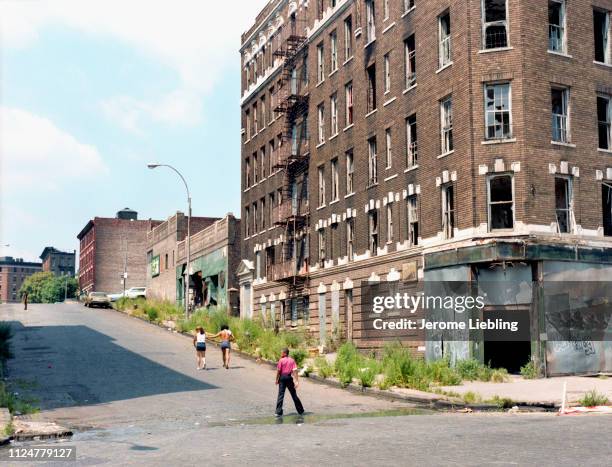 Wide profile view of an unidentified young man standing in the street in front of a bombed-out abandoned building in New York City's impoverished...