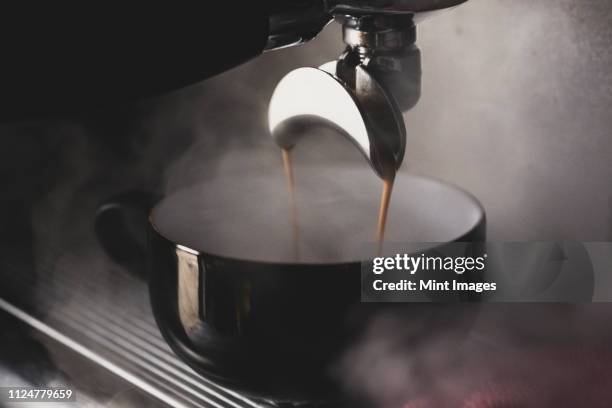 close up of black mug on espresso machine, hot coffee pouring from spout. - coffee maker stock pictures, royalty-free photos & images