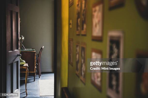 view along corridor with vintage pictures on green wall, open brown wooden door to study with antique desk and chair. - domestic room photos stock pictures, royalty-free photos & images
