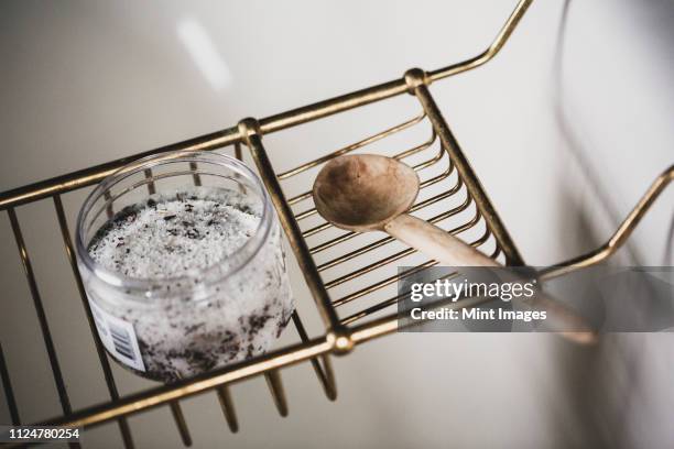 high angle close up of jar of bath salts and wooden spoon on brass bath caddy. - bath salt stock pictures, royalty-free photos & images