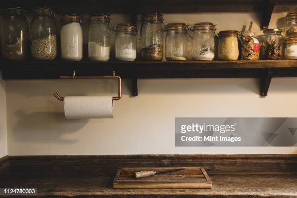 wooden chopping board and knife on vintage wooden kitchen cupboard, row of glass jars with cooking ingredients on a wooden shelf. - jars kitchen stock pictures, royalty-free photos & images