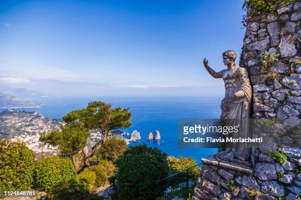 statue of tiberius in capri island with a view of faraglioni rocks, italy - capri imagens e fotografias de stock