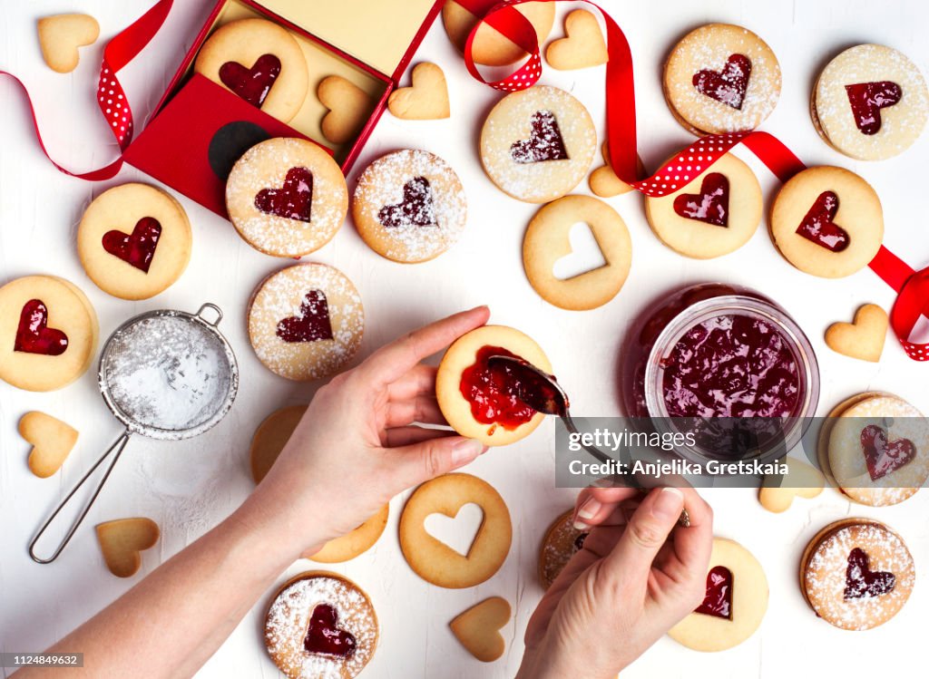 Traditional Linzer cookie with strawberry jam, top view. Female hands making cookies.