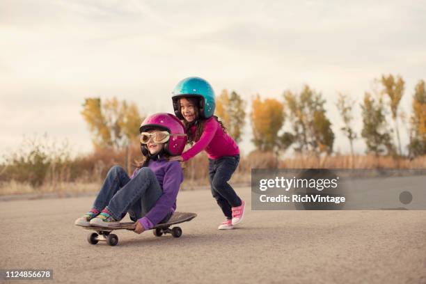 zwei mädchen auf einem skateboard rennen - pushing stock-fotos und bilder