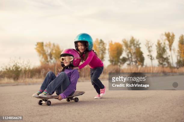 two girls racing on a skateboard - kids playing imagens e fotografias de stock
