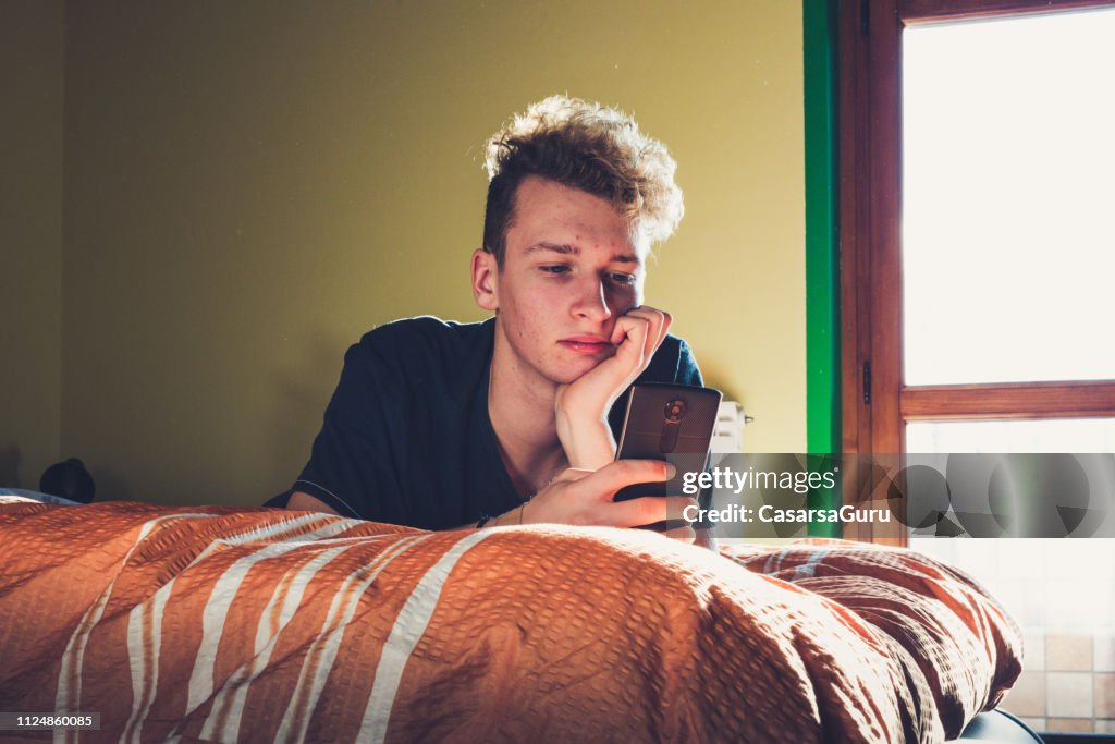 Teenager mit seinem Smartphone beim Verlegen auf dem Bett