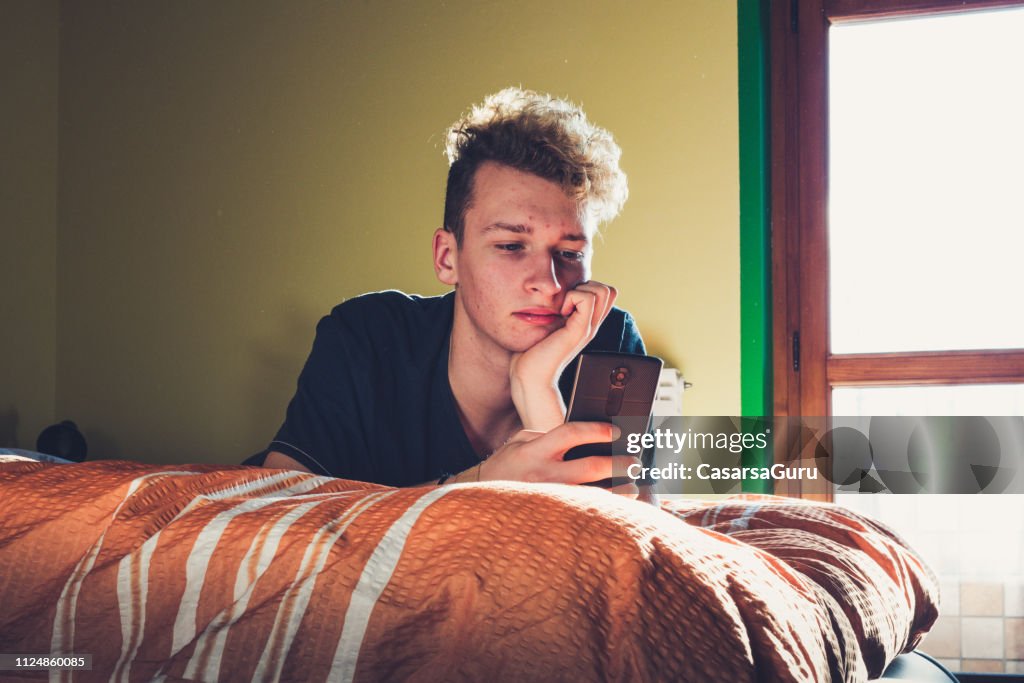 Tiener met behulp van zijn slimme telefoon terwijl leggen op het Bed
