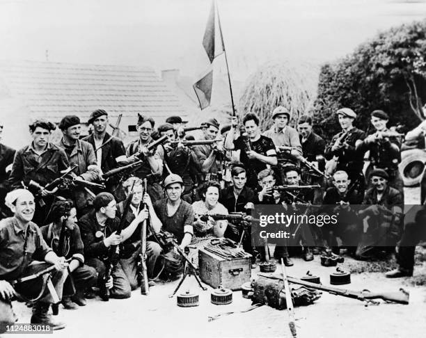 Group of French resistance fighters pose for a picture with weapons and a flag in the courtyard of a farm in France, in an indeterminate place,...