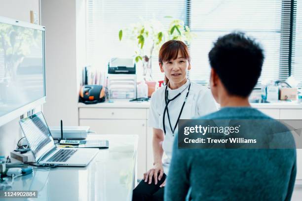 mature female doctor consulting with a mid adult man at a hospital - medical examination room stock pictures, royalty-free photos & images