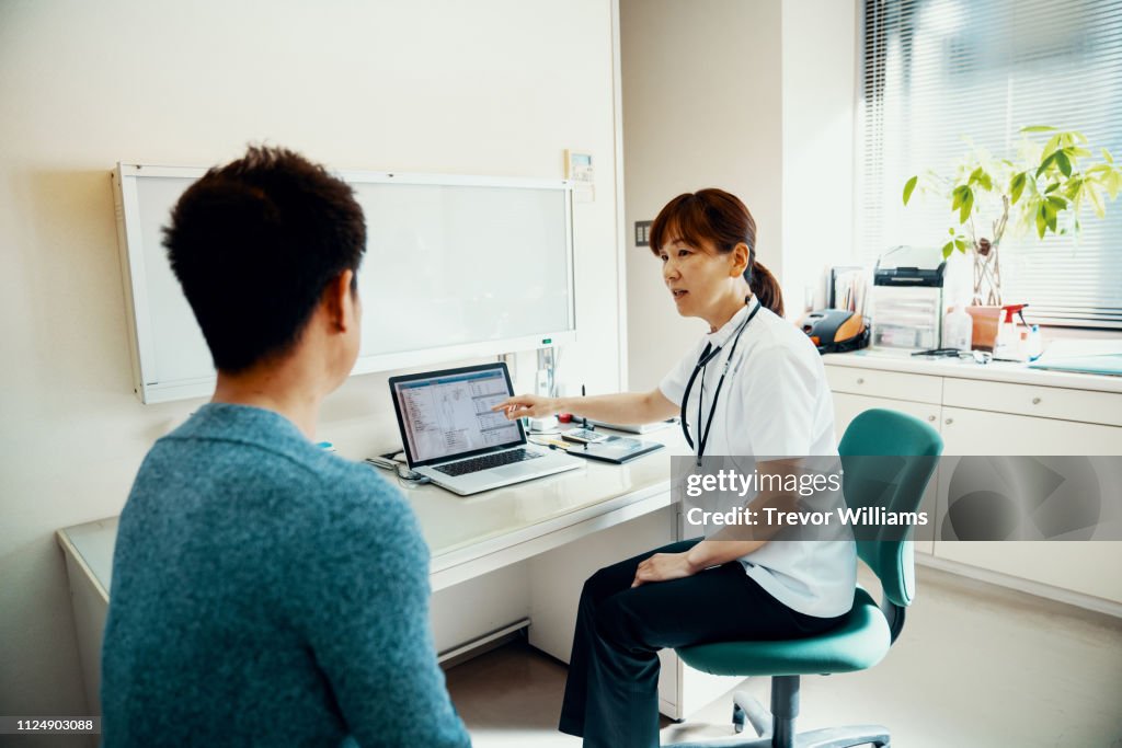 Mature female doctor discussing medical test results with a mid adult man while pointing at a computer screen