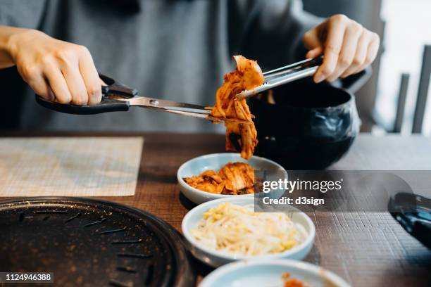 close up of woman serving fresh kimchi on plate while having meal in a korean restaurant - kimchi stock pictures, royalty-free photos & images