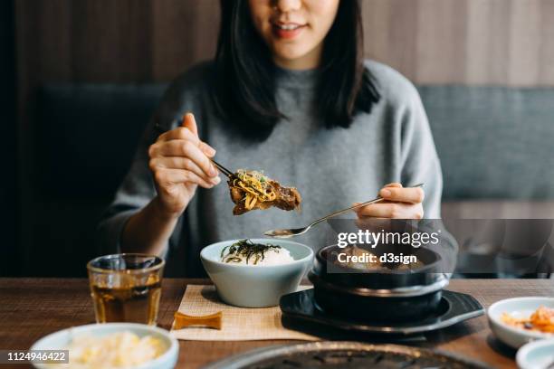 smiling young asian woman enjoying traditional korean cuisine in a korean restaurant - korean food stockfoto's en -beelden