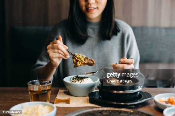 smiling young asian woman enjoying traditional korean cuisine in a korean restaurant - korean food stock pictures, royalty-free photos & images