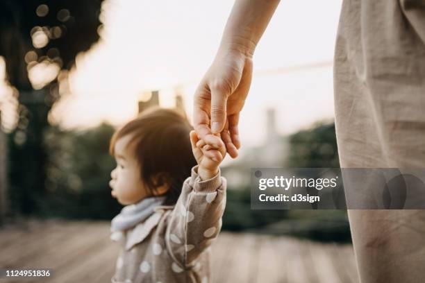 cute baby girl holding mother's hand having a relaxing walk in the park at sunset - child hand stockfoto's en -beelden