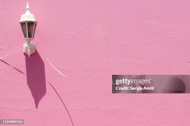 wall lamp casting a shadow on a pink wall - bo kaap stock-fotos und bilder