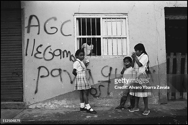 Children standuing by graffiti on a wall in Policarpa, translated as: "AGC [Autodefensas de Colombia] we have come to stay." Over the past month this...