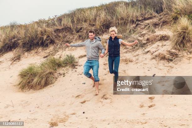 glückliches paar hand in hand, die von den sanddünen auf fistral beach, newquay, cornwall auf ein herbsttag. - couple dunes stock-fotos und bilder