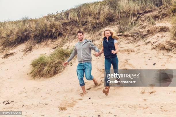 gelukkige paar hand in hand loopt van de duinen op fistral beach, newquay, cornwall op een dag van de herfst. - couple dunes stockfoto's en -beelden