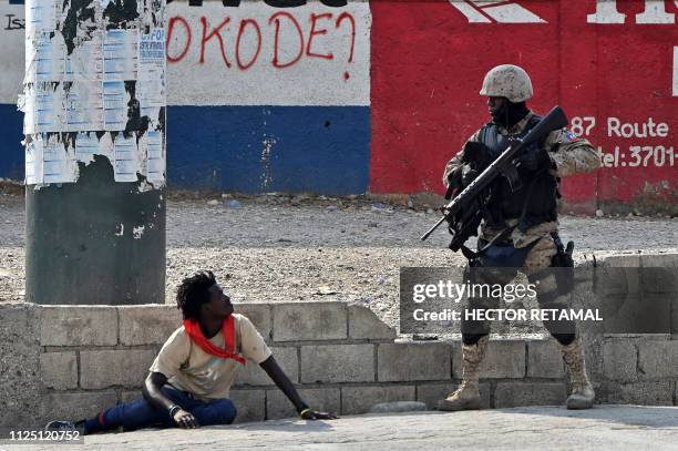 Haitian police officer inspect a man nearby the International Airport, in Port-au-Prince, on February 15 on the ninth day of protests against Haitian...