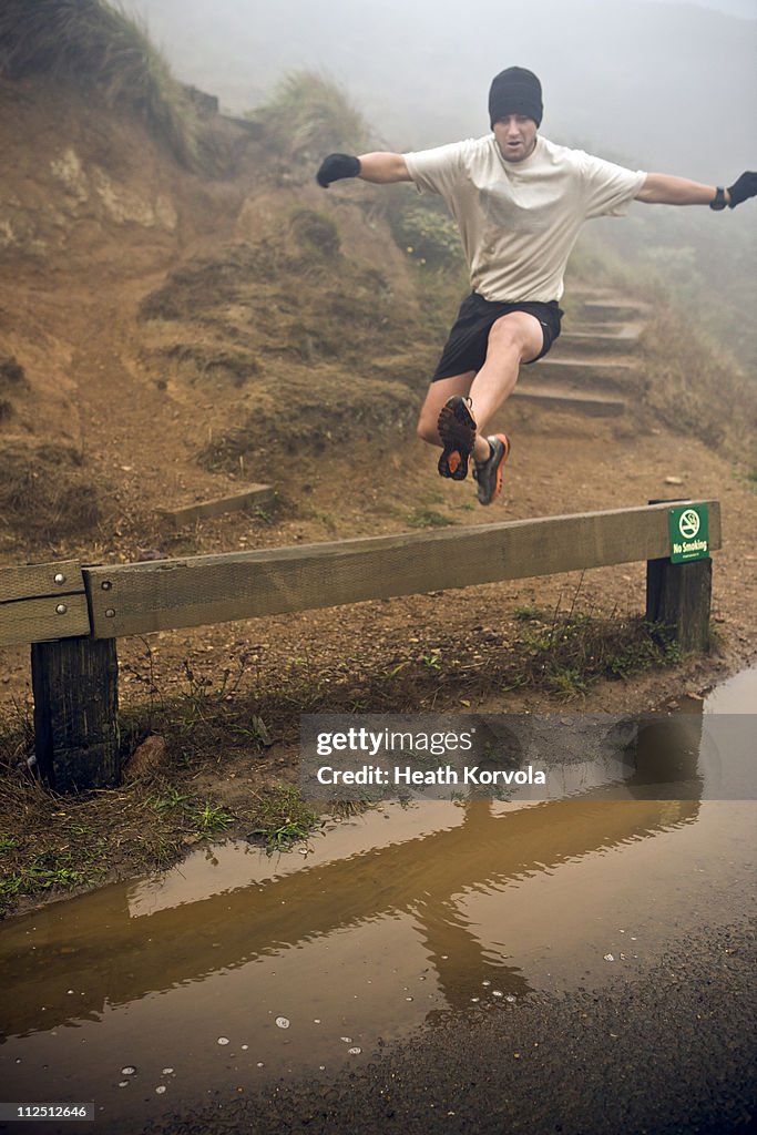 Man jumping over barrier while on trail run.