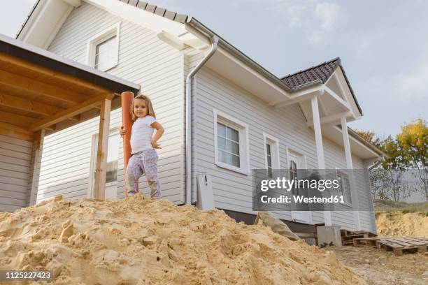 happy blond girl standing on heap of sand near construction site of a detached one-family house - einfamilienhaus stock-fotos und bilder