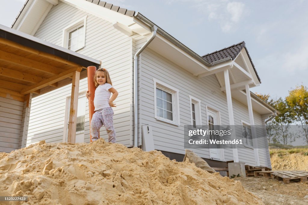 Happy blond girl standing on heap of sand near construction site of a detached one-family house