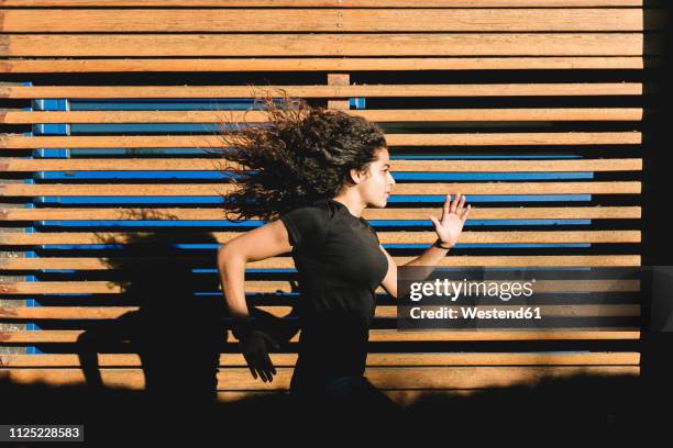 sportive young woman running along wood paneling - sprinting stock pictures, royalty-free photos & images