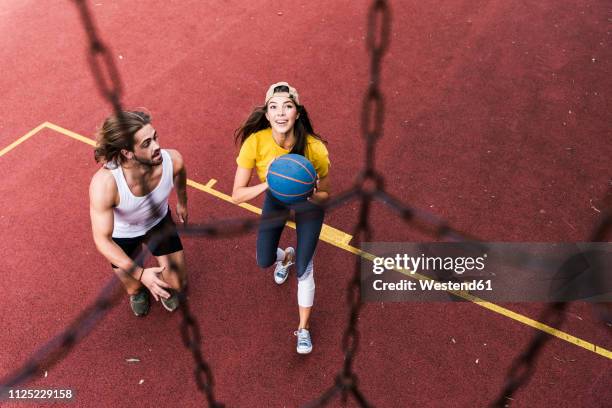 young man and woman playing basketball on basketball ground - womens basketball stock-fotos und bilder