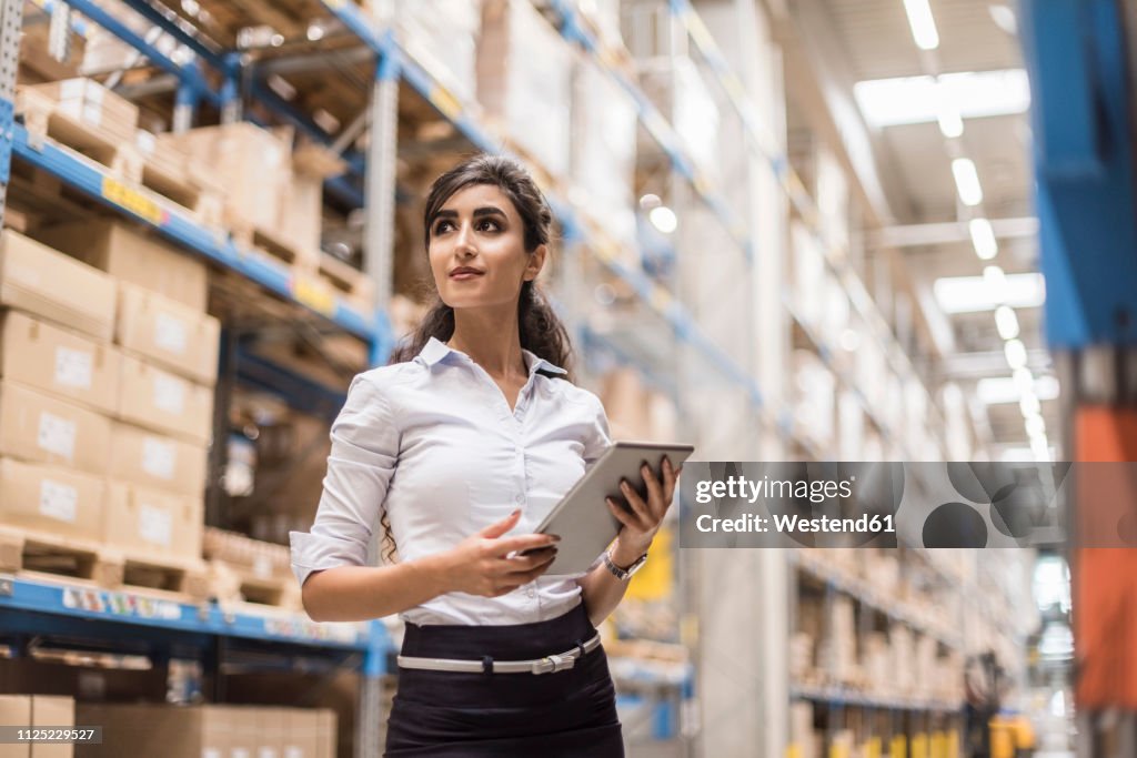 Woman with tablet in factory storehouse looking around