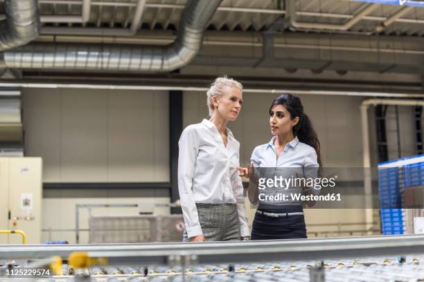 two women discussing at conveyor belt in factory - garment industry stock pictures, royalty-free photos & images