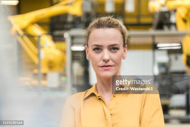portrait of confident woman in factory shop floor with industrial robot - goud metaal stock pictures, royalty-free photos & images
