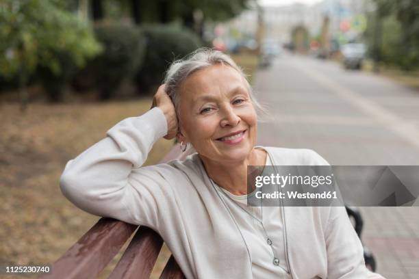 portrait of smiling senior woman relaxing on a bench - white bench stock pictures, royalty-free photos & images