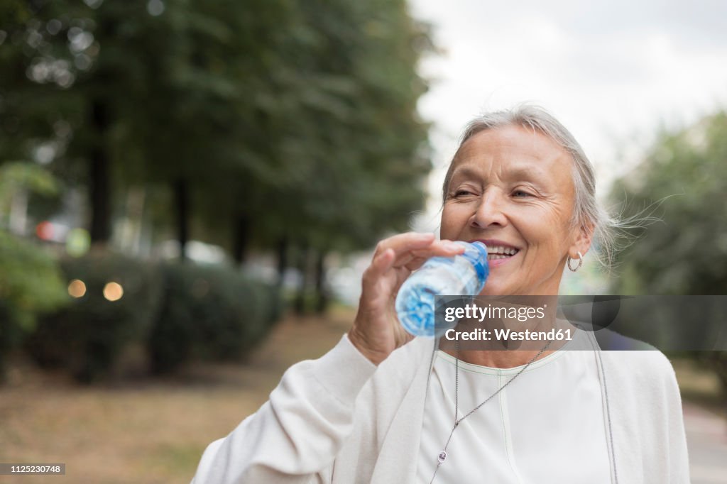 Happy senior woman outdoors drinking water from bottle