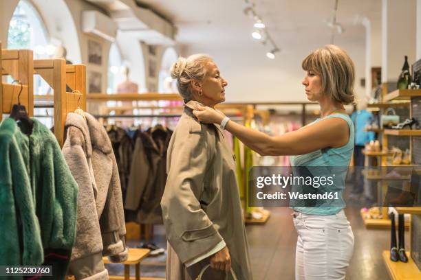 senior woman trying on coat in a boutique - essayer photos et images de collection