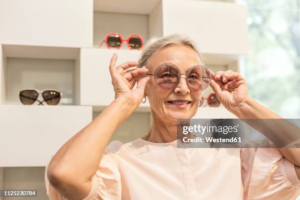 smiling senior woman trying on sunglasses in a boutique - frau mit sonnenbrille stock-fotos und bilder