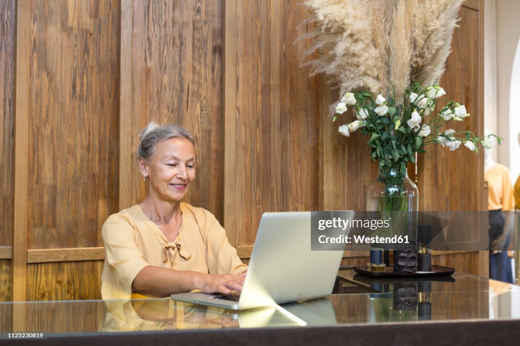 Smiling senior woman using laptop at reception desk