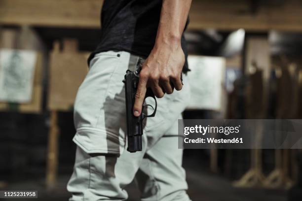 close-up of man holding a pistol in an indoor shooting range - armi da fuoco foto e immagini stock